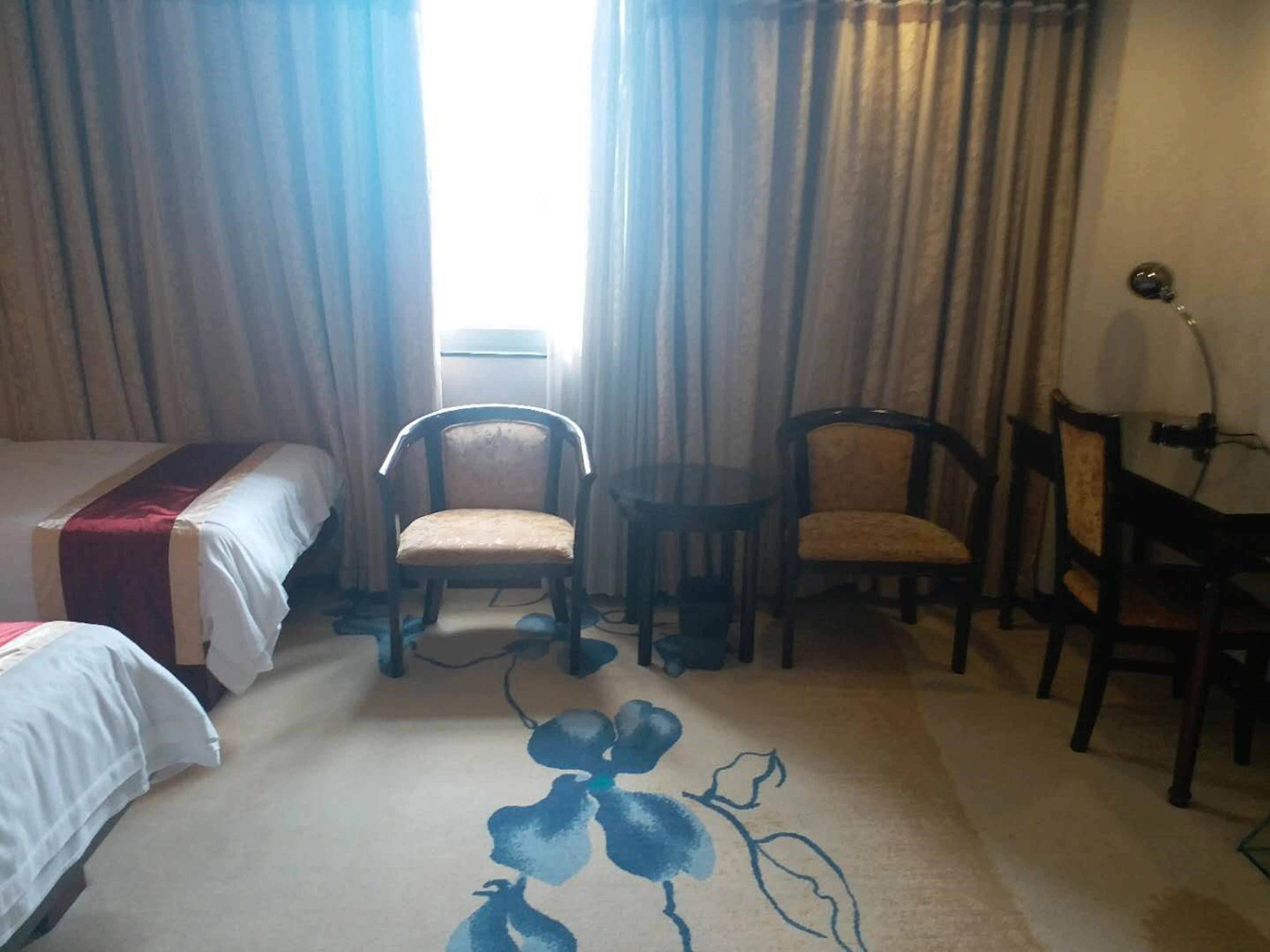 A hotel room with a bed, two chairs, a small table, and a window with curtains.