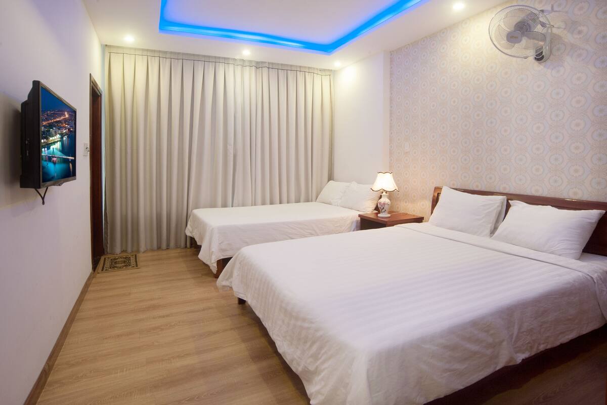 A hotel room with two beds, a TV, a ceiling fan, and a view of the city at night.