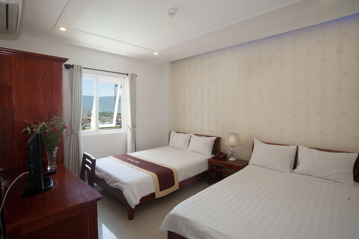 A hotel room with two beds, a desk with a computer, a window with curtains, and a view of the outside.