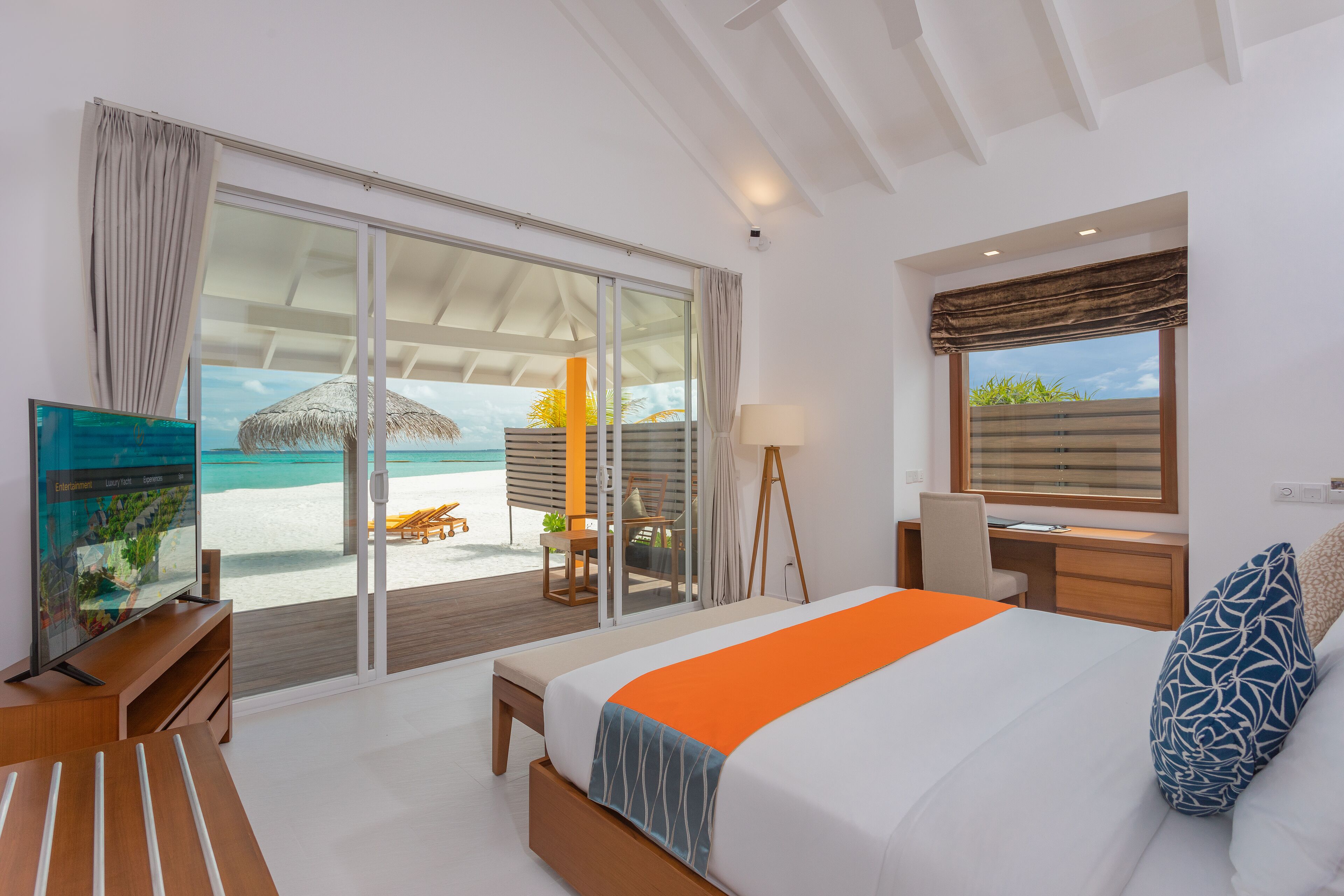 A modern hotel room with a large bed, a desk, a chair, and a view of the beach.