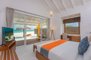 A modern hotel room with a large bed, a desk, a chair, and a view of the beach.