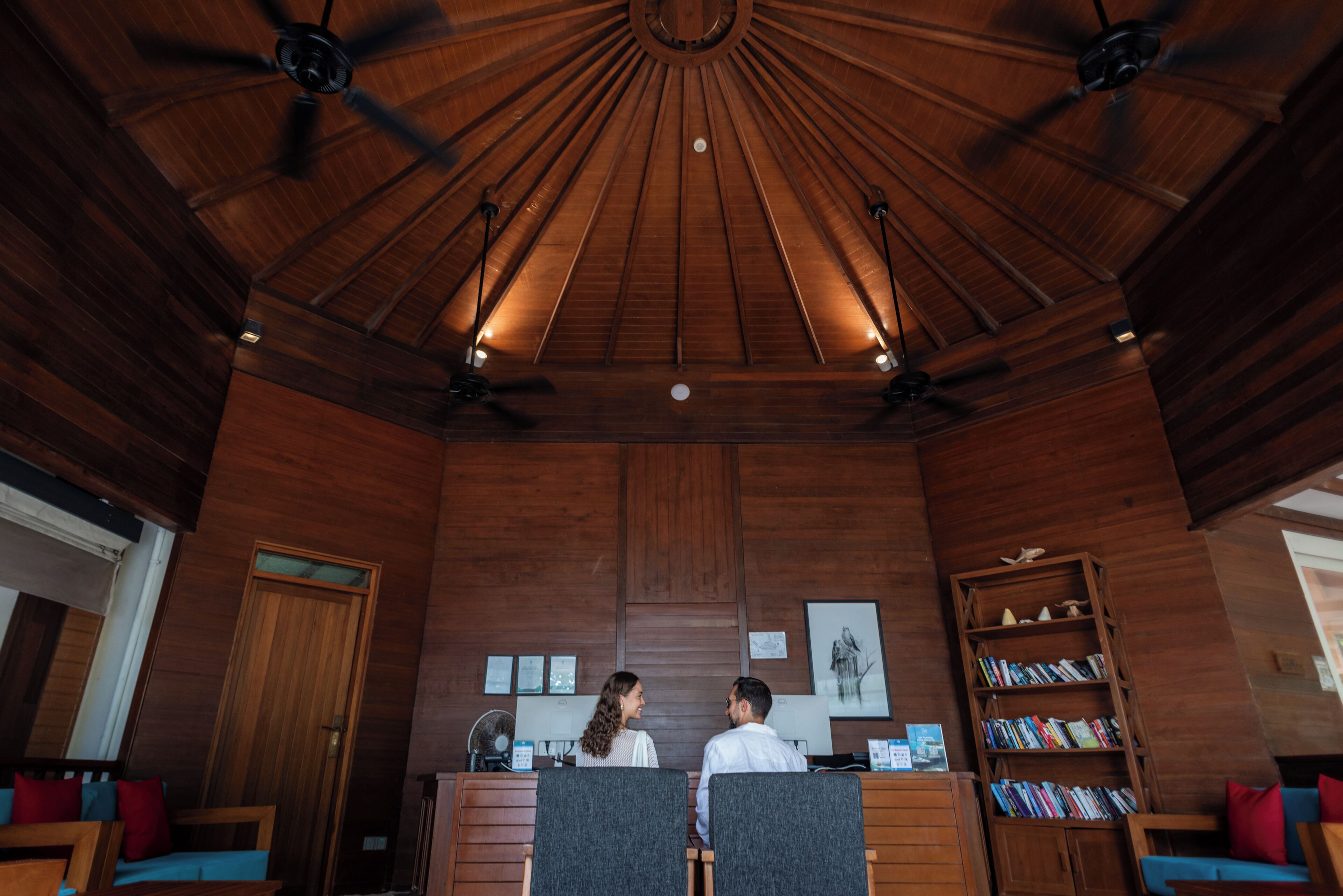 A reception area with wooden paneling, ceiling fans, a reception desk, and a bookshelf.