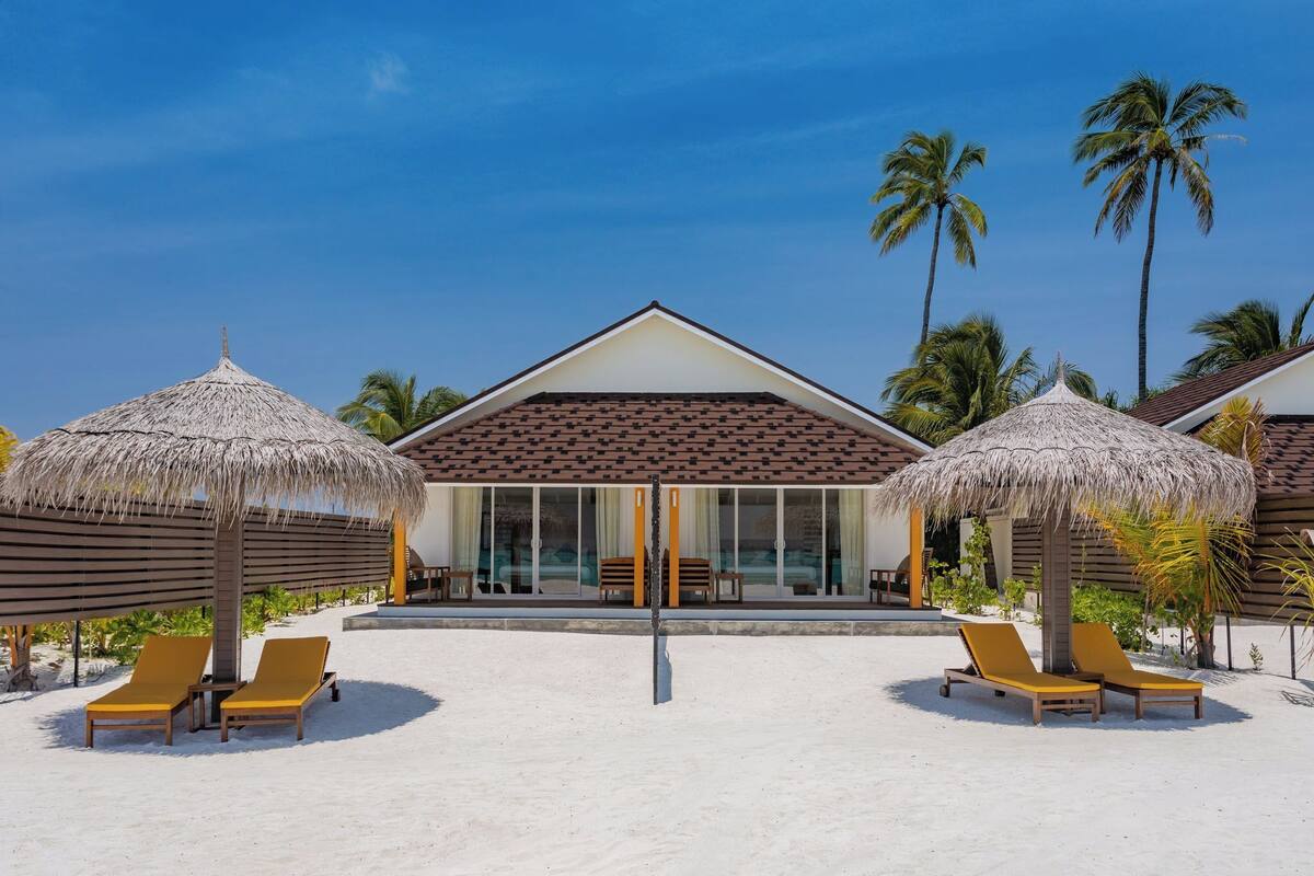 Ein Strandhotel mit Reetdachschirmen, Liegestühlen und Palmen.