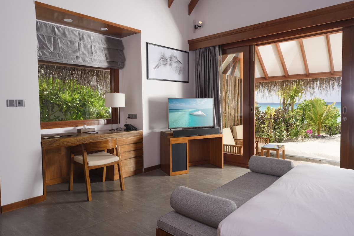 Ein Hotelzimmer mit Bett, Schreibtisch mit Computer, Fernseher und Blick auf den Strand.