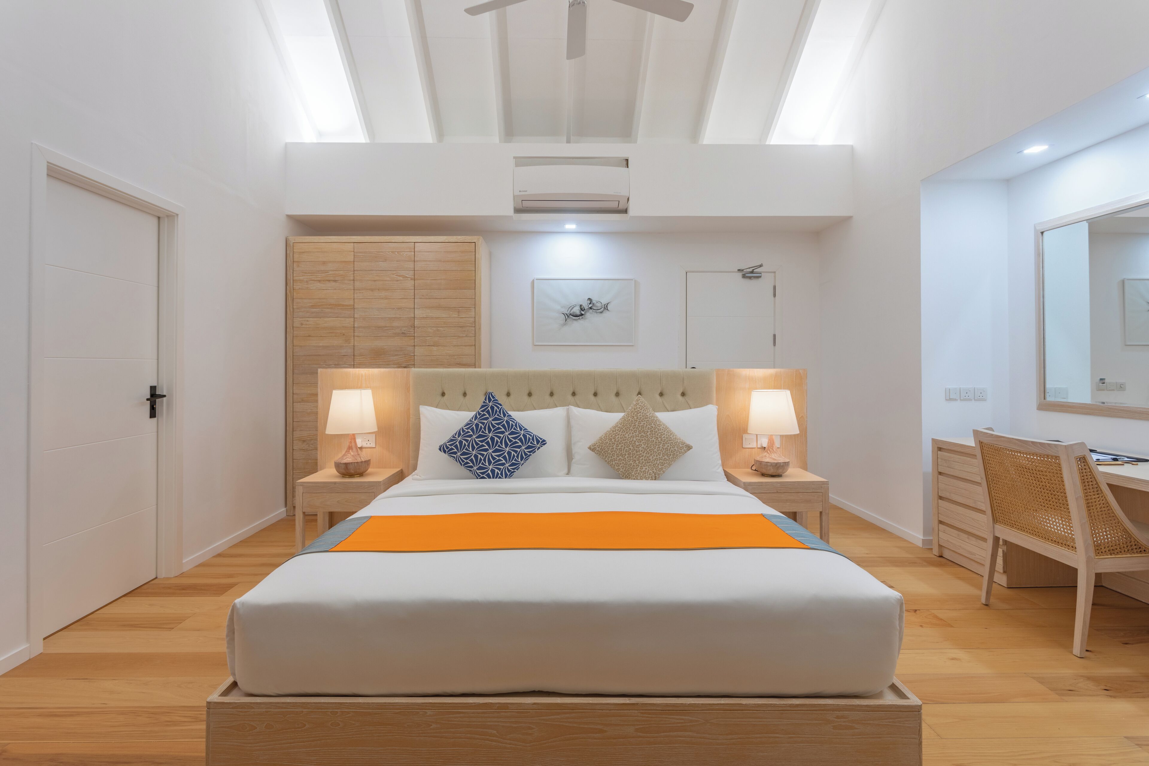 A modern bedroom with a large bed, two bedside tables with lamps, a wooden wardrobe, a desk with a chair, and a ceiling fan.