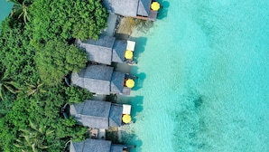 Vista aérea de un resort con bungalows sobre el agua, aguas turquesas cristalinas y exuberante vegetación.