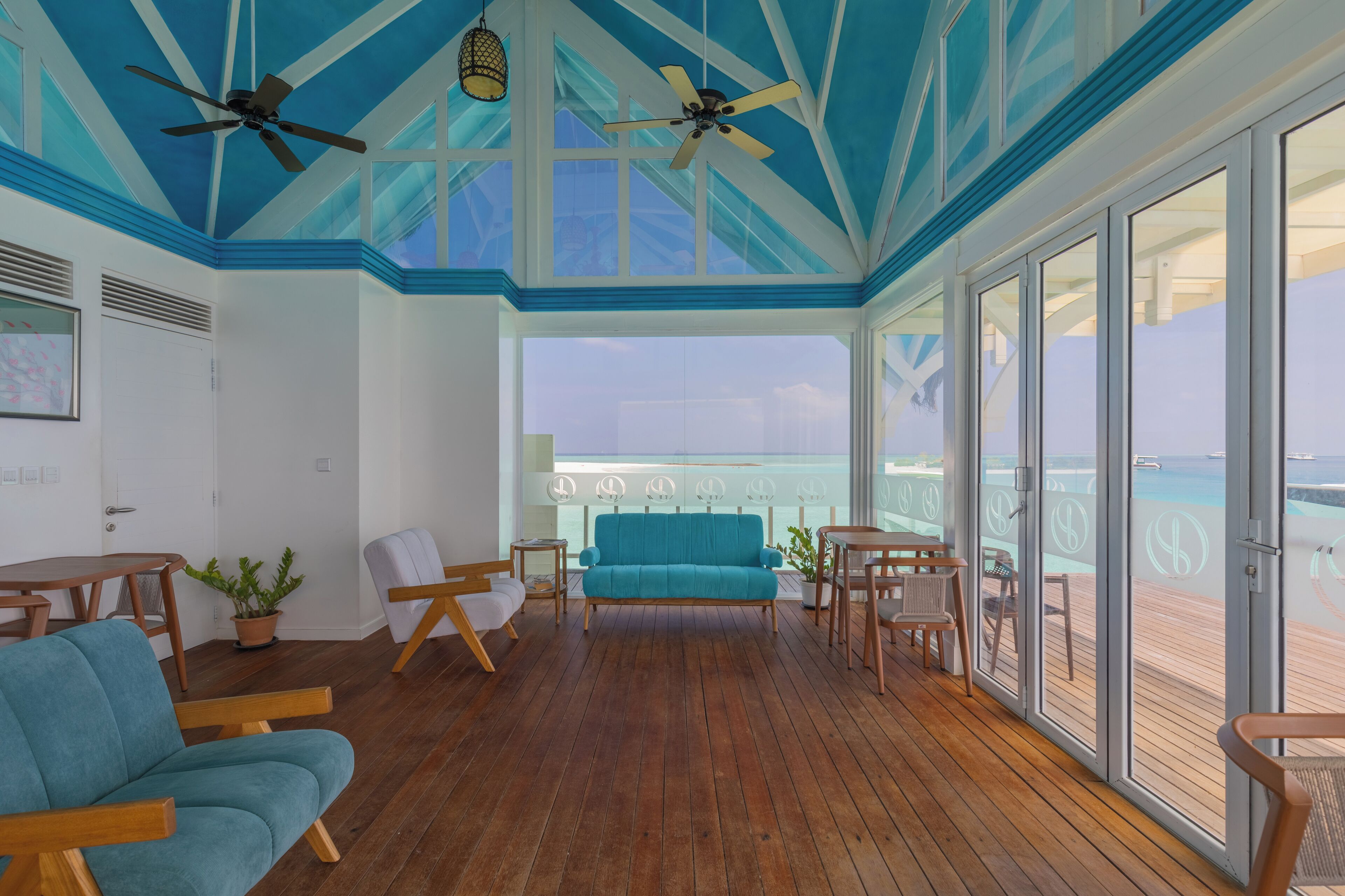 Un balcon spacieux doté d’un plancher en bois, d’un canapé de couleur turquoise et de deux ventilateurs de plafond.