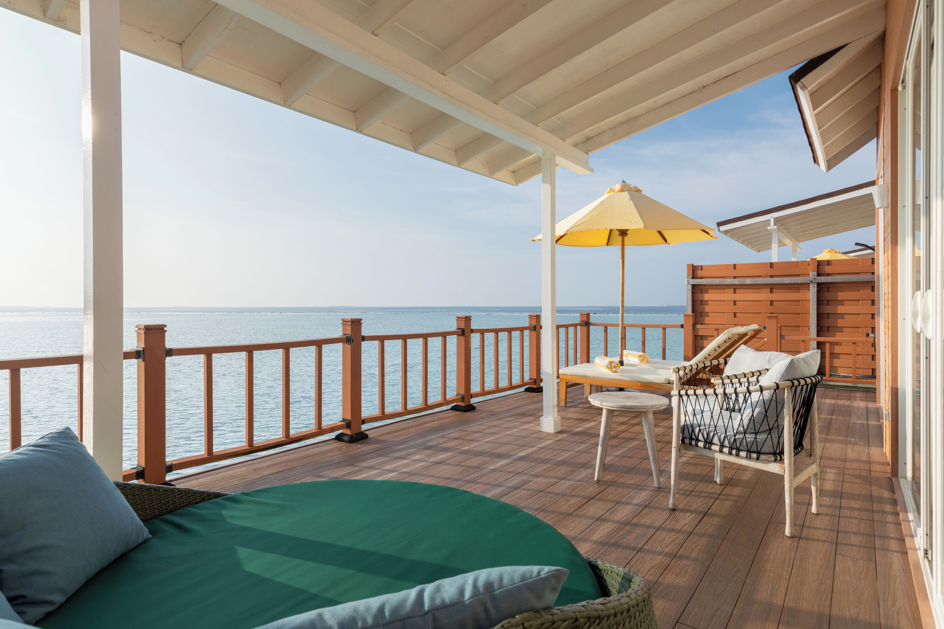 A deck with a view of the sea, a bed, a wicker chair, and a table with an umbrella.