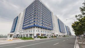 Un immeuble moderne de grande hauteur, doté de nombreux balcons, donnant sur une rue urbaine propre et bien aménagée.