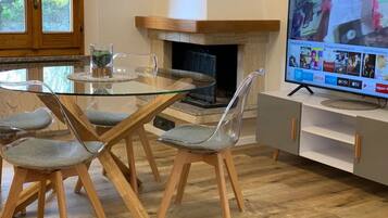 Uma sala de estar moderna com uma mesa de jantar de vidro, cadeiras transparentes, lareira e uma televisão de tela plana montada em um armário.