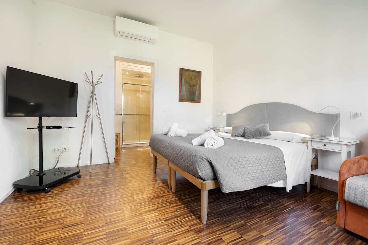 A modern hotel room with a bed, bedside table, TV, and a shower area.