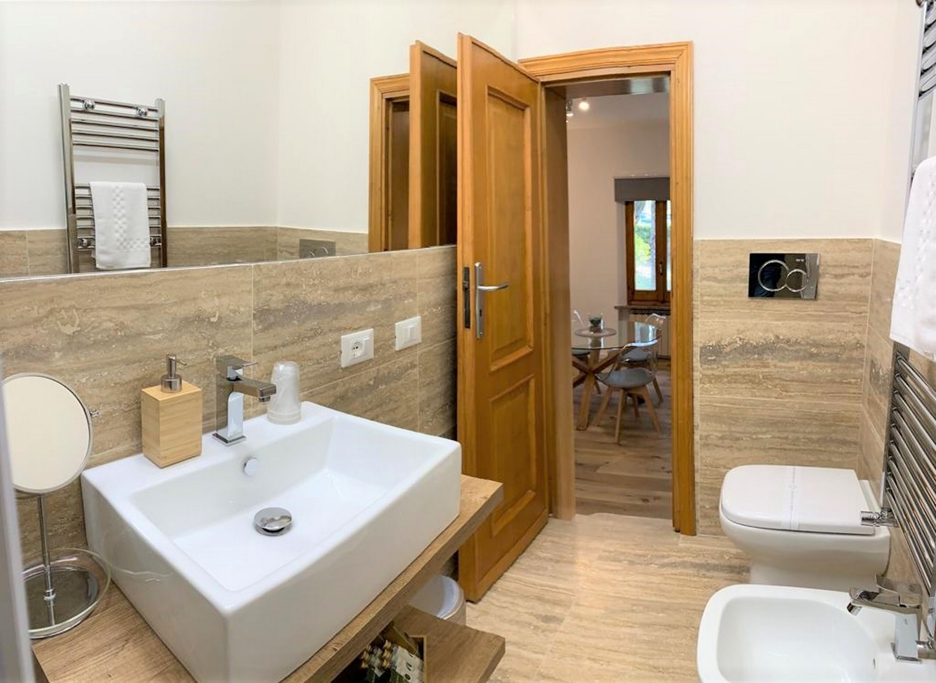 Une salle de bain moderne avec un grand lavabo, des toilettes et un bidet. Une porte en bois donne accès à un coin repas.