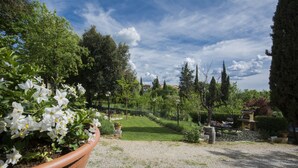 Un jardín con un sendero de grava, plantas en macetas y una mesa de piedra.