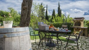 Un patio al aire libre con una mesa redonda, sillas, una parrilla y un barril.
