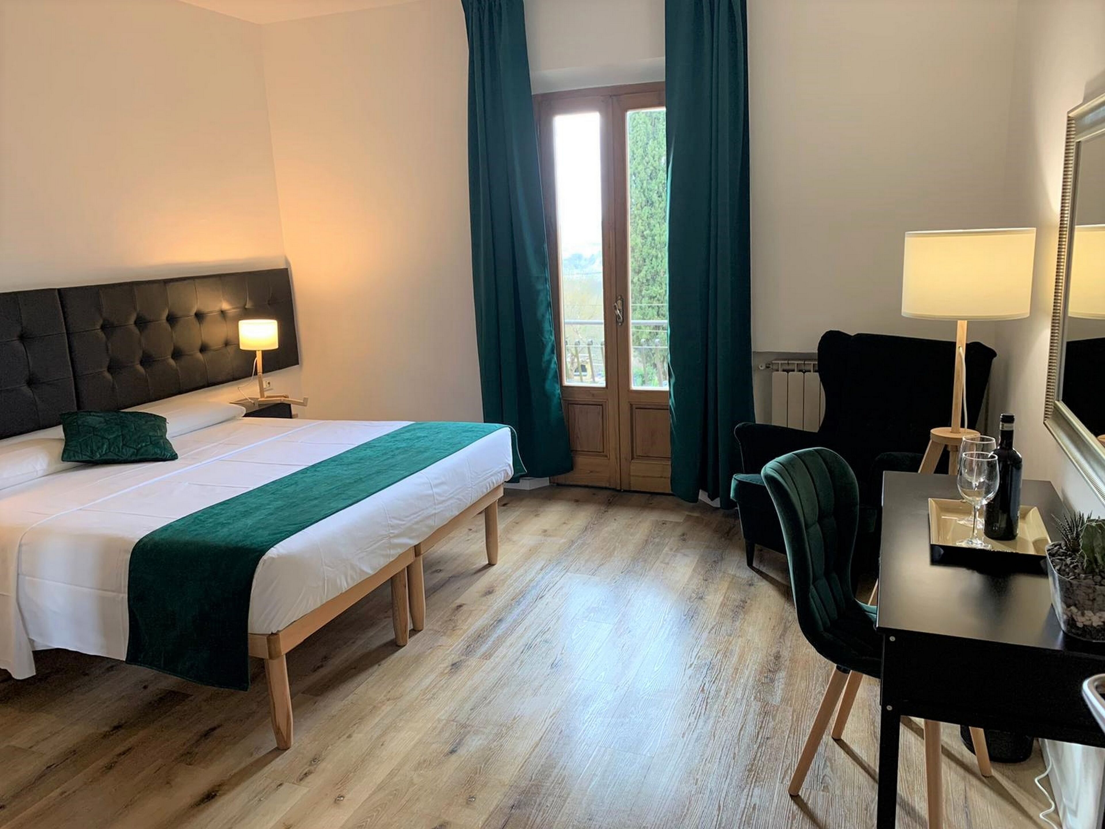 A hotel room with a bed, a desk, a chair, a lamp, and a window with curtains.