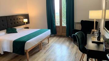 A hotel room with a bed, a desk, a chair, a lamp, and a window with curtains.