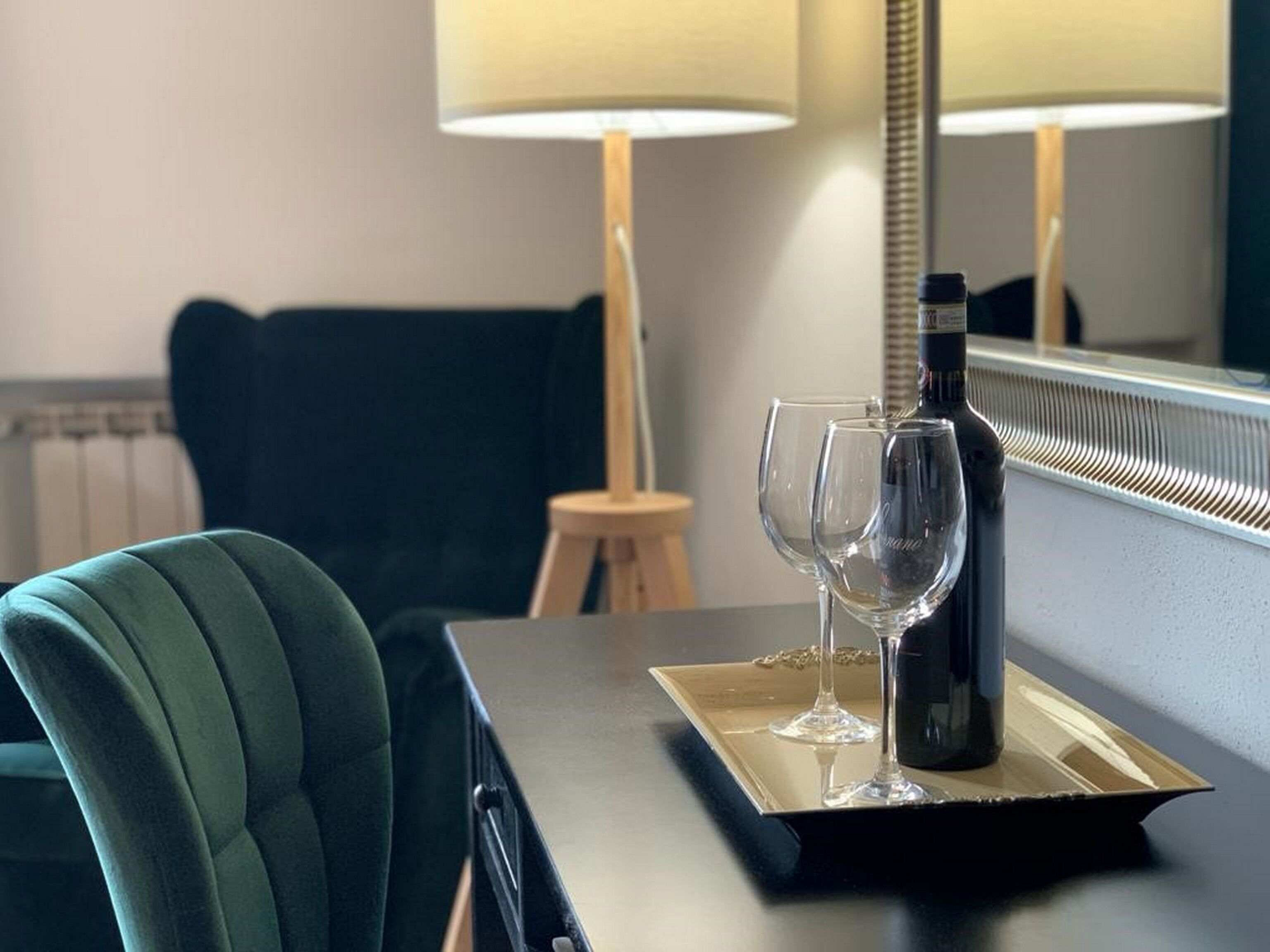 Een hotelkamer met een donkergroene fauteuil, een klein houten krukje en een dienblad met een fles en twee glazen.