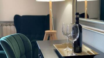 Een hotelkamer met een donkergroene fauteuil, een klein houten krukje en een dienblad met een fles en twee glazen.
