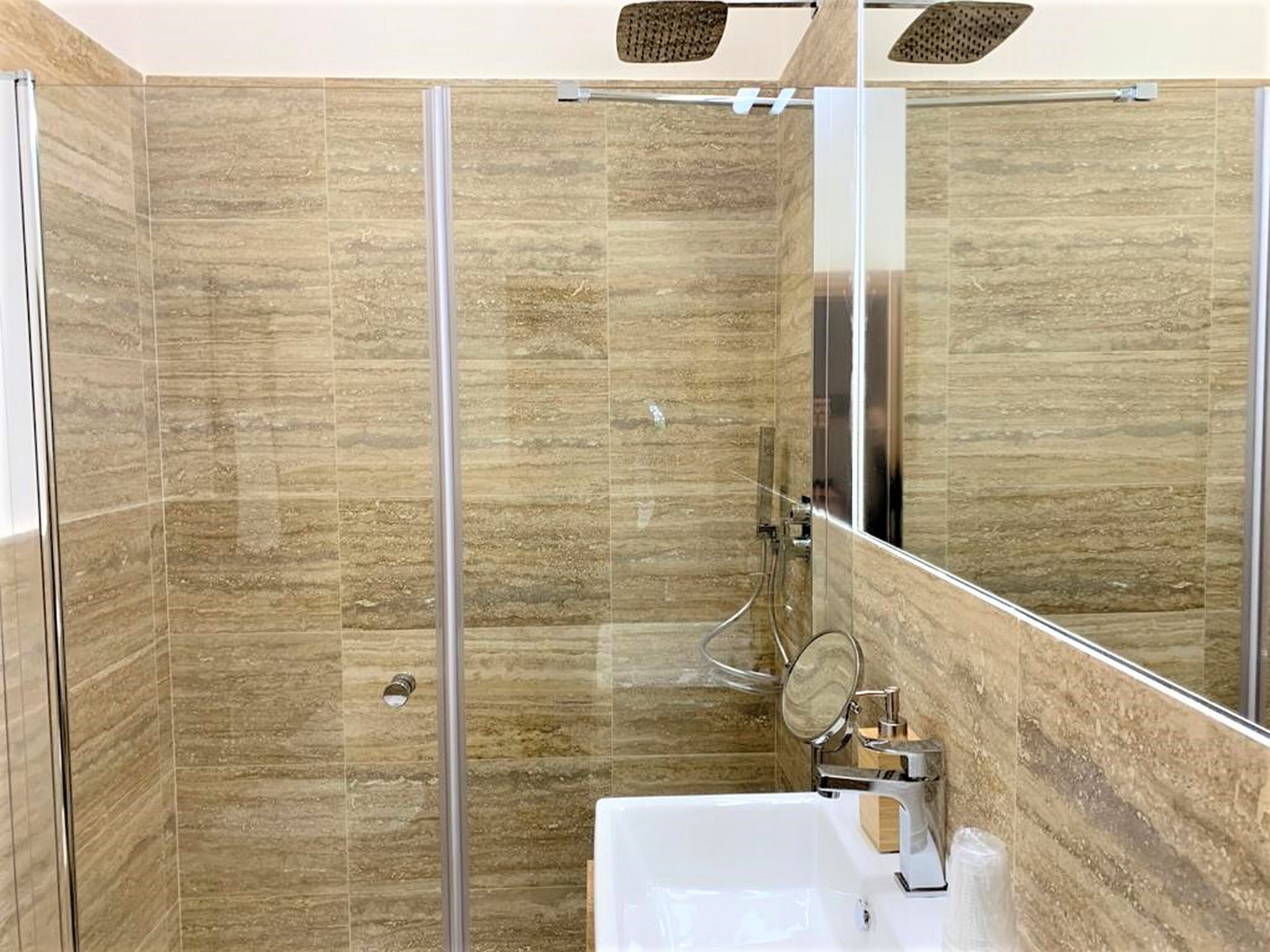 Une salle de bain moderne avec une douche à l’italienne en verre, un lavabo blanc et un grand miroir.