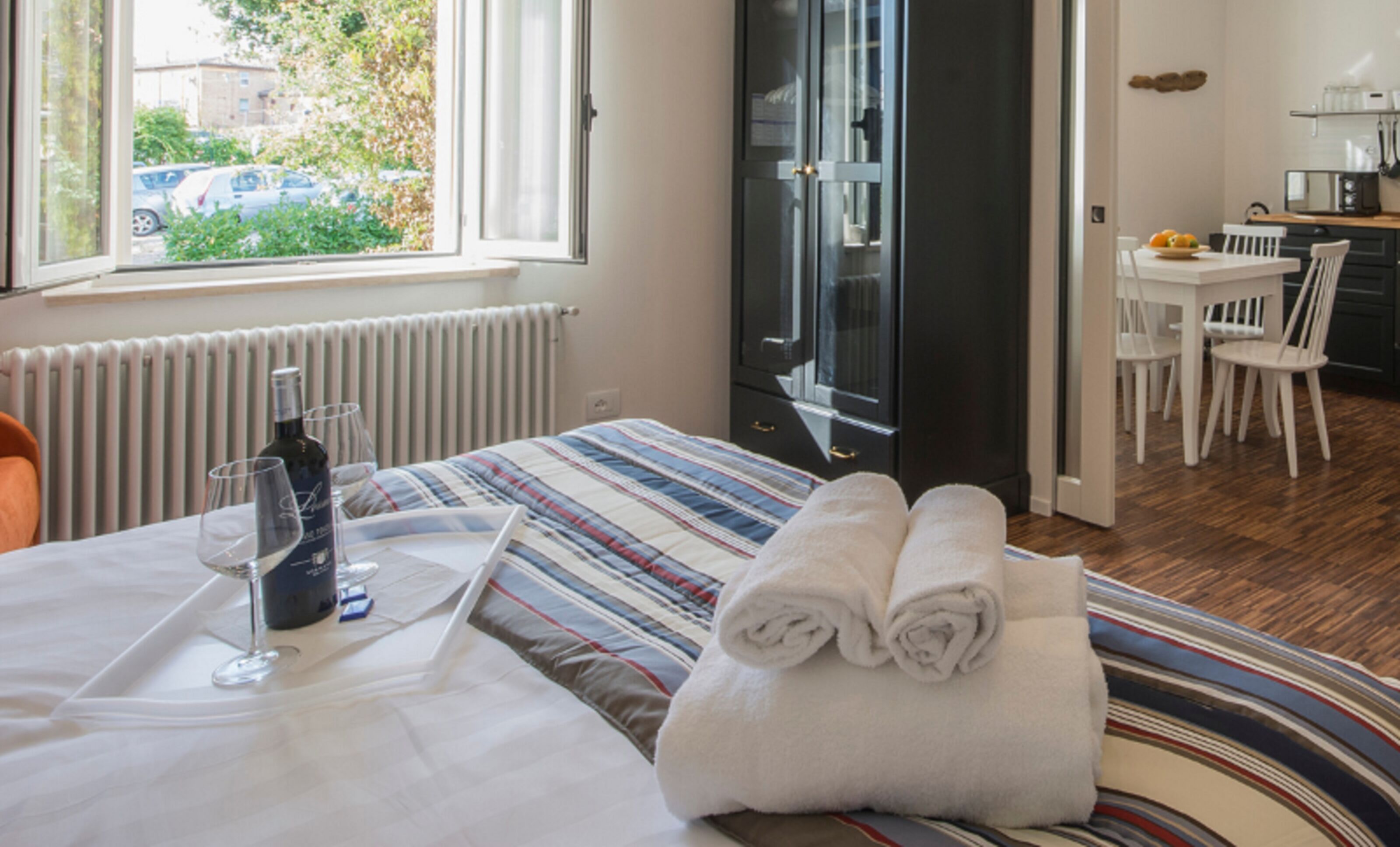 A hotel room with a bed, a dining table with chairs, a kitchen area, and a view of the outside.