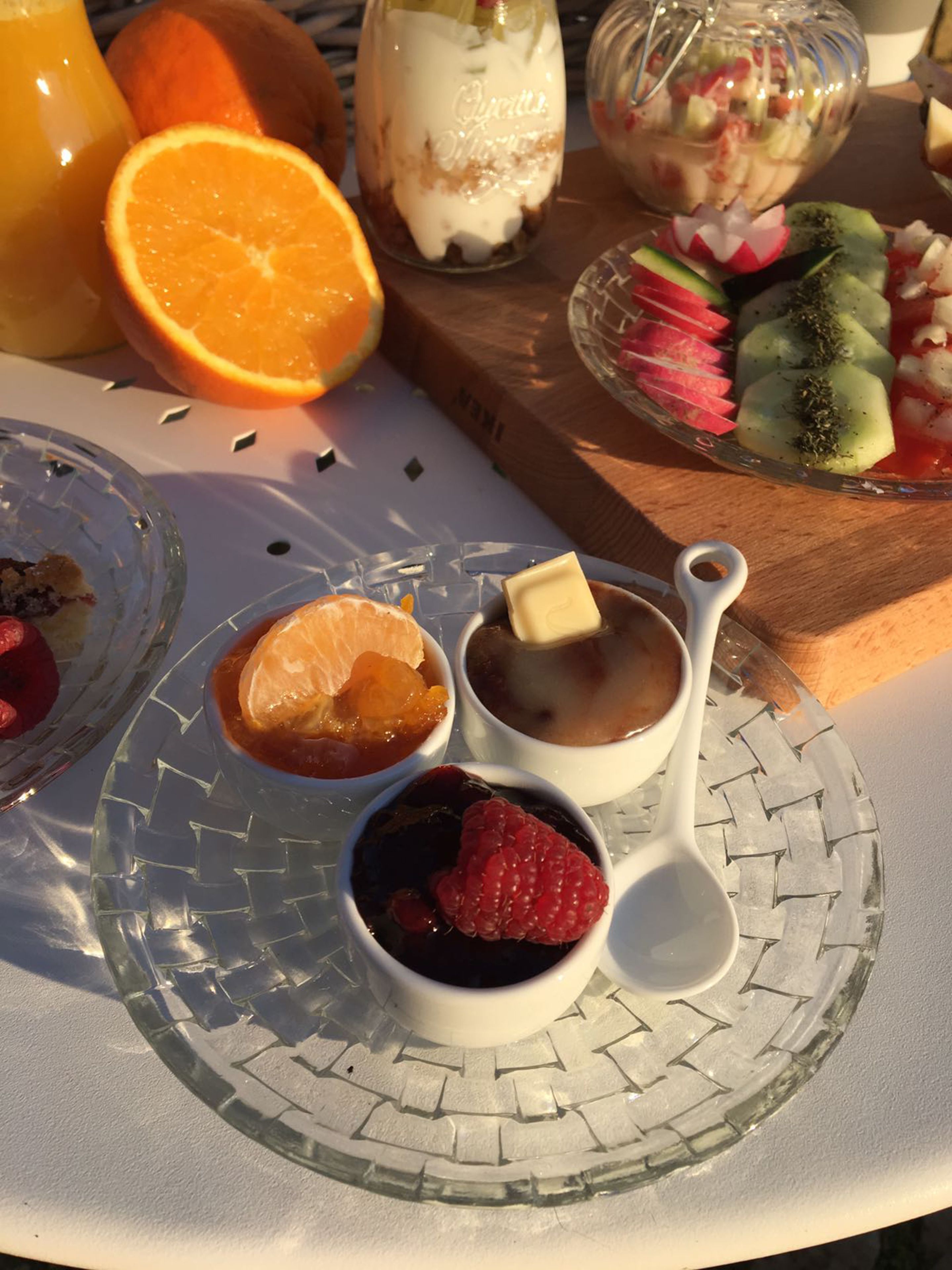 Mesa de café da manhã com diversas frutas, um copo de suco de laranja e uma tigela de parfait de iogurte.