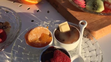 Mesa de café da manhã com diversas frutas, um copo de suco de laranja e uma tigela de parfait de iogurte.