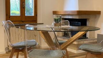 Een eetgedeelte met een tafel met glazen blad, vier stoelen met metalen frame, een houten kast en een open haard.