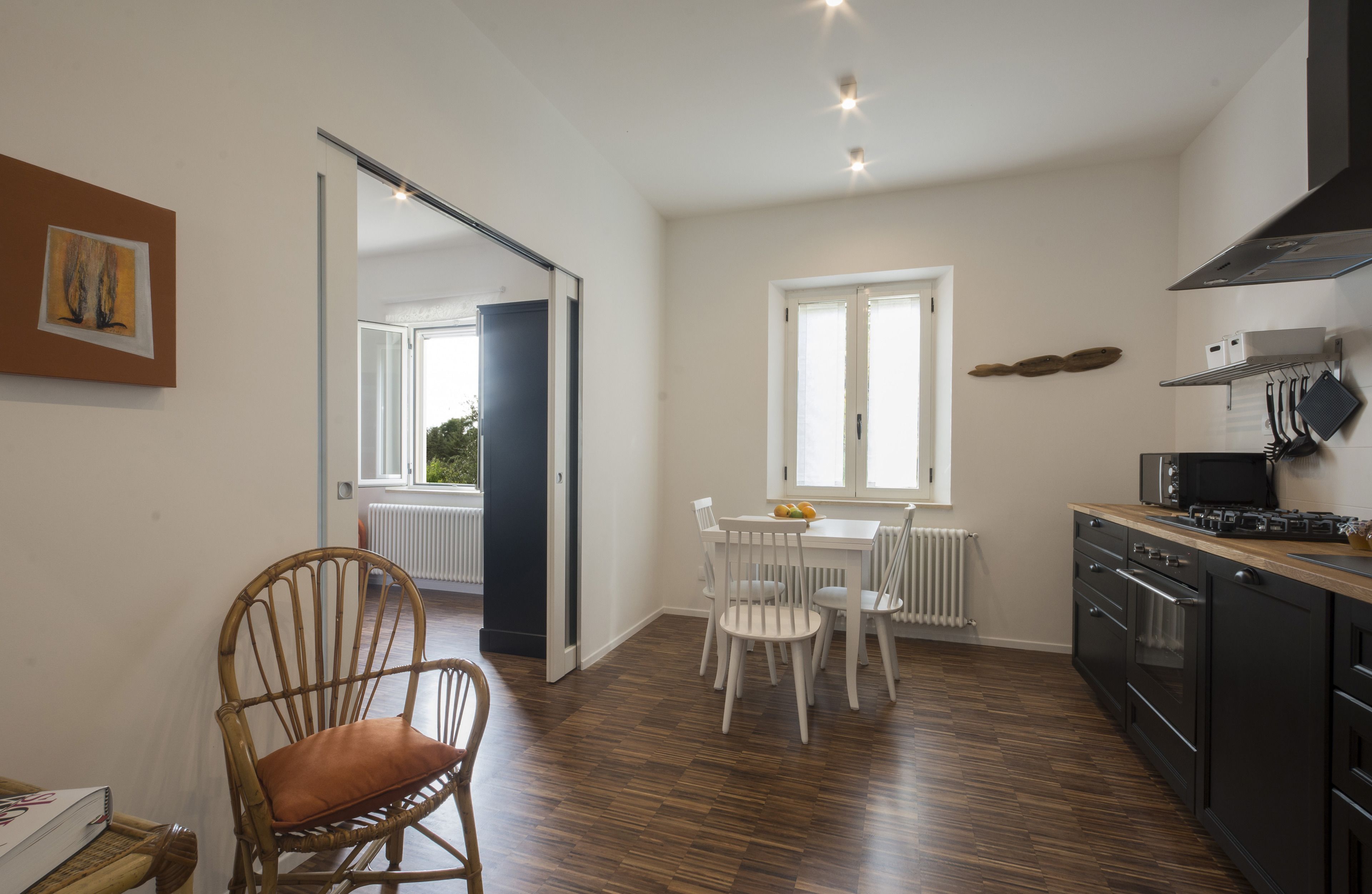 A modern kitchen with a dining area, wooden flooring, and a view through an open door.
