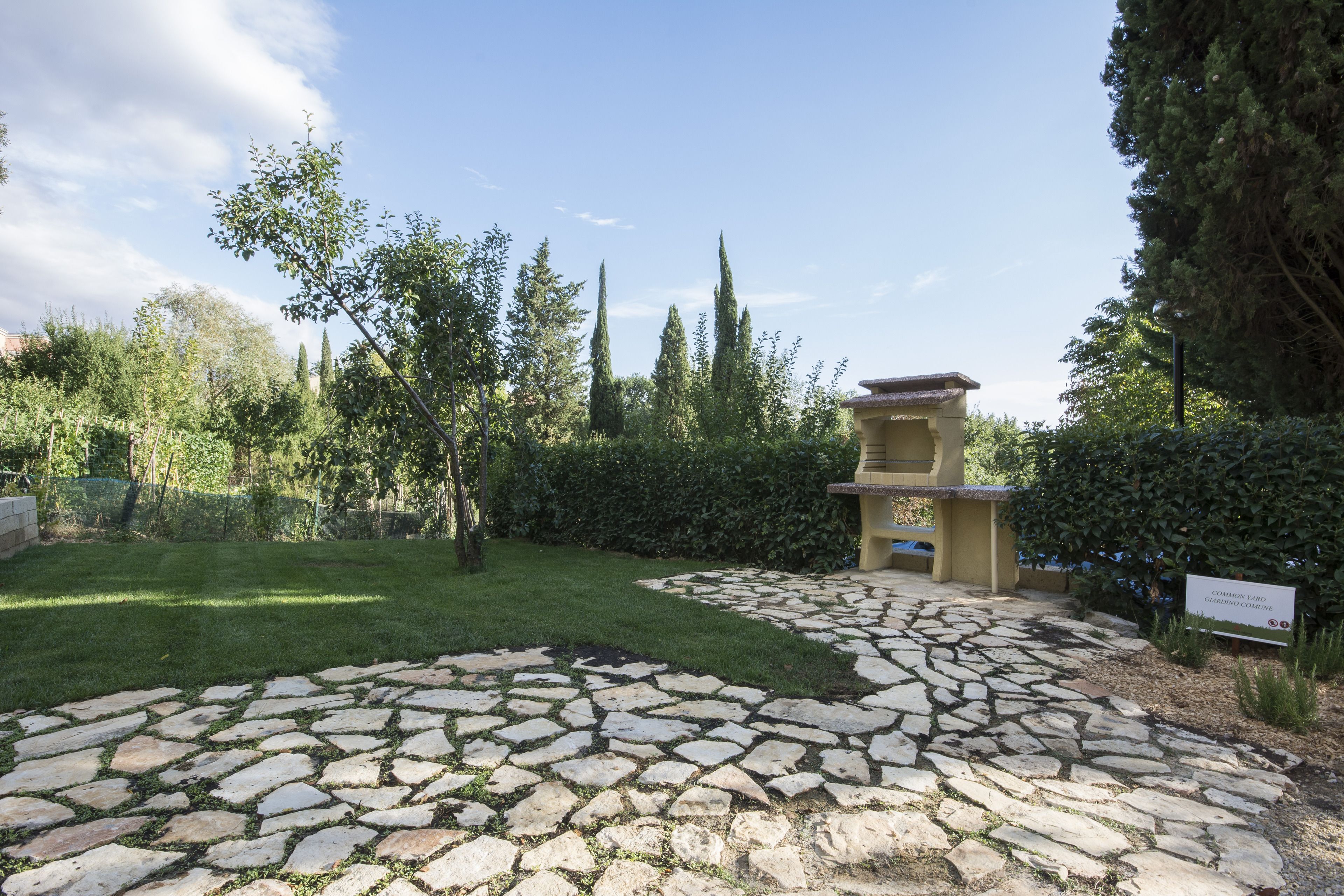 A stone pathway leading to a gazebo in a landscaped garden with trees and a clear sky.