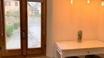 Een kamer met een houten deur, een raam met uitzicht op een binnentuin, een witte toonbank met een plant en twee groene, beklede zitplaatsen.