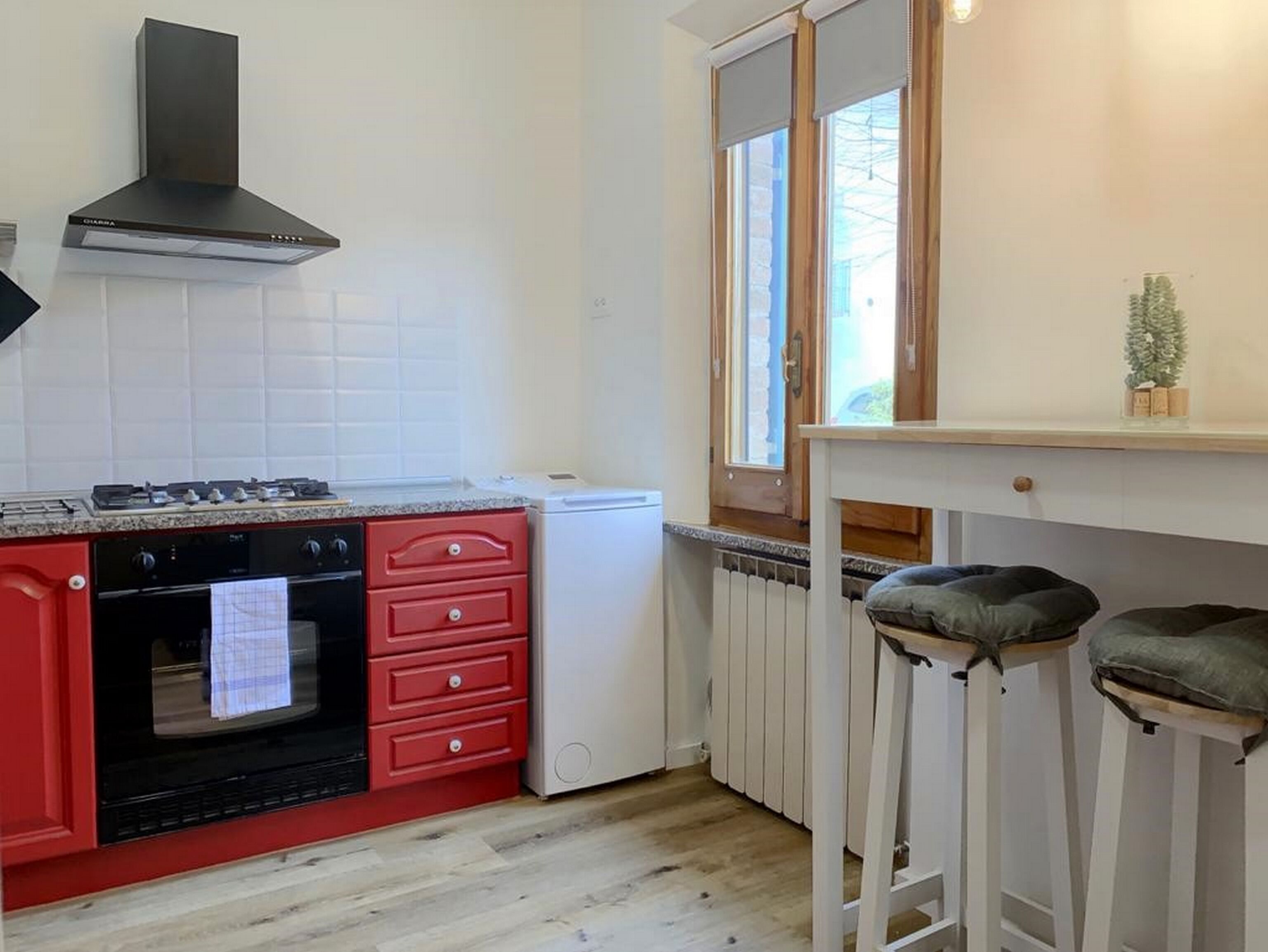 A compact kitchen with a gas stove, red cabinetry, a white refrigerator, and a window with blinds.