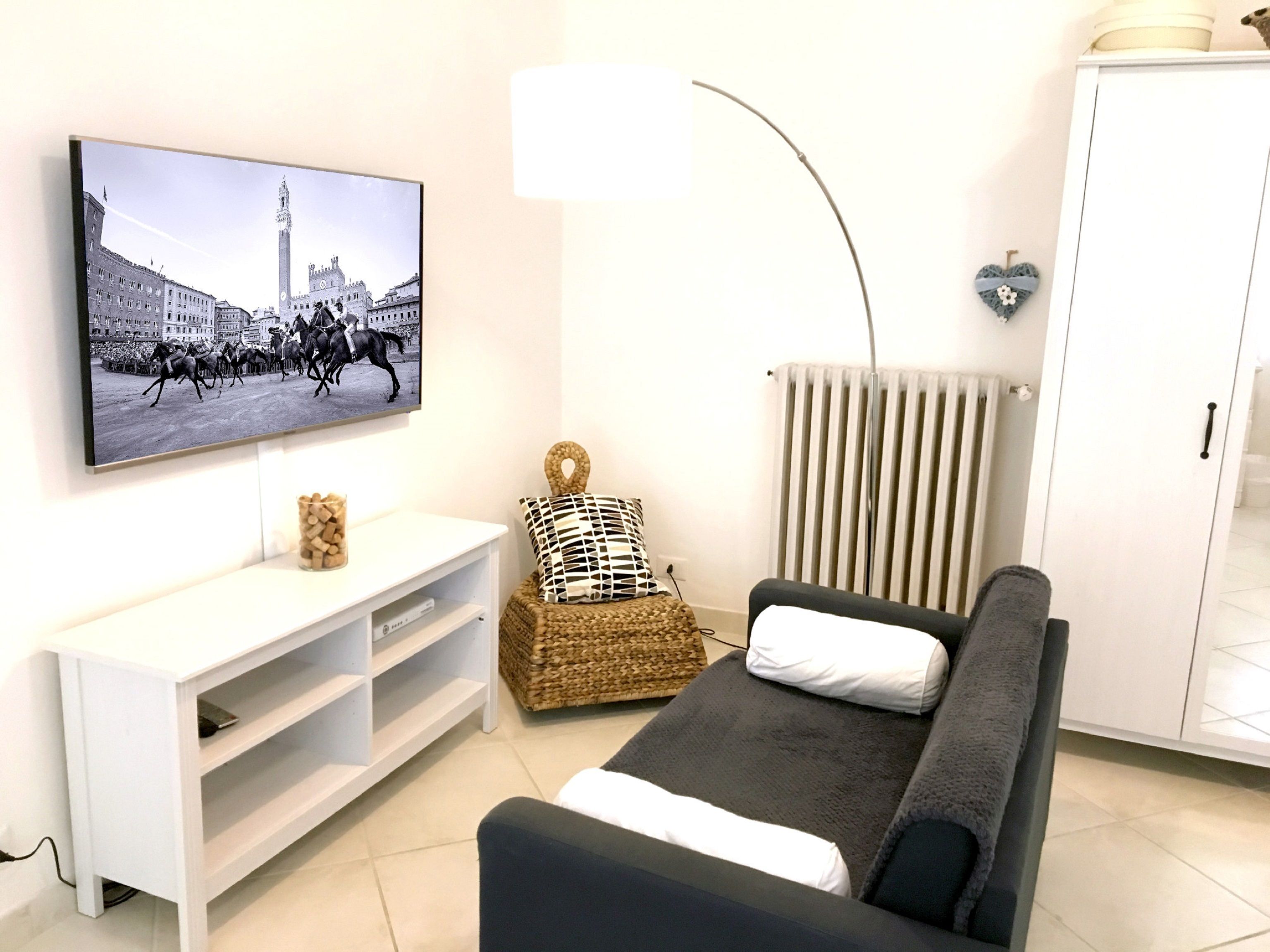 Ein Wohnzimmer mit Flachbildfernseher an der Wand, einer Couch, einer weißen Unterhaltungsanlage, einem Heizkörper und einem Schrank.