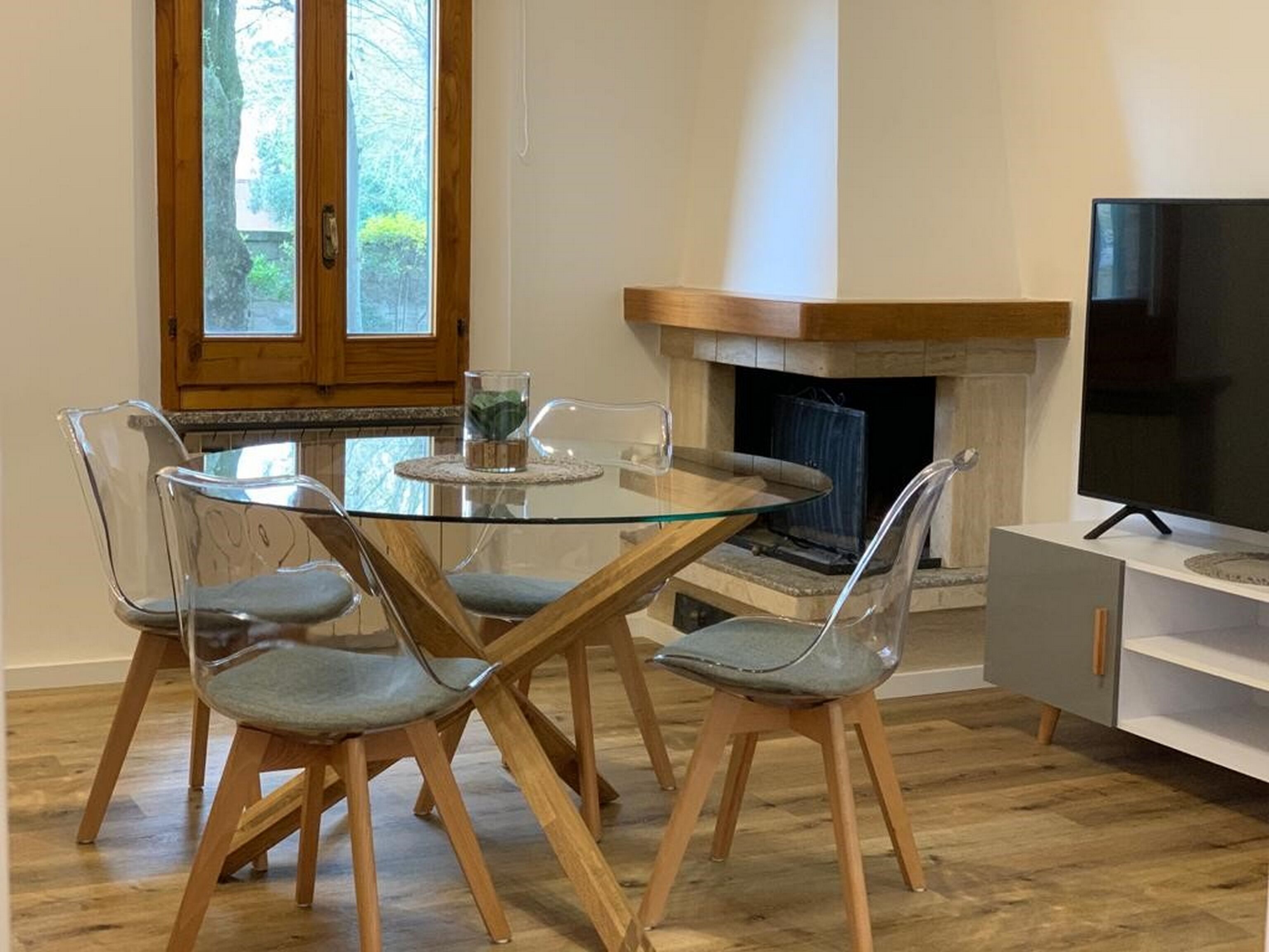 A dining area with a glass table and chairs, a fireplace, and a television.