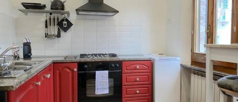 A kitchen with red cabinets, a black stove, and a white refrigerator.