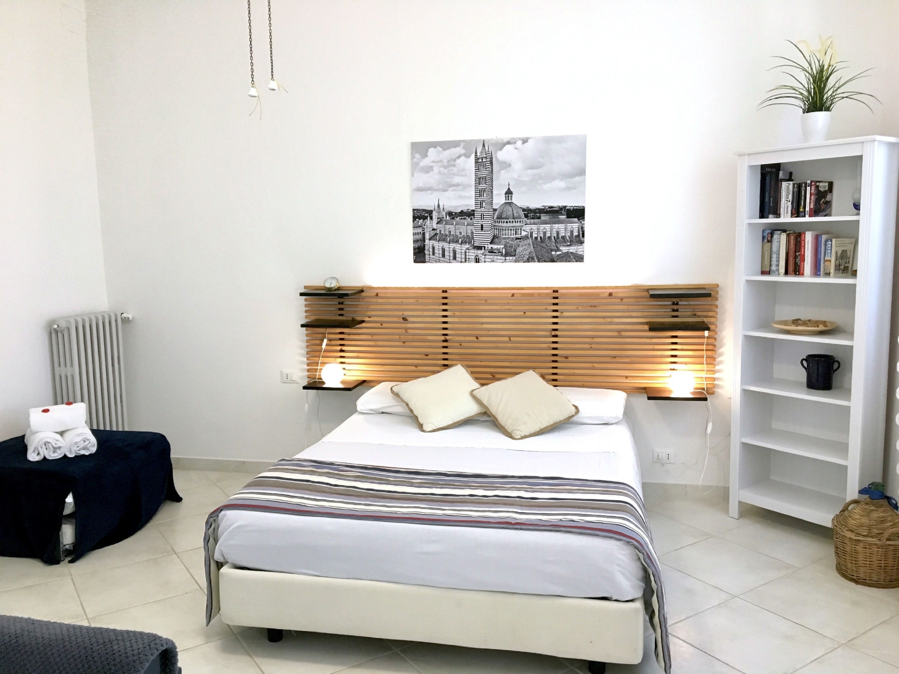 Une chambre à coucher moderne, avec un lit, une table de chevet, une bibliothèque et un radiateur.