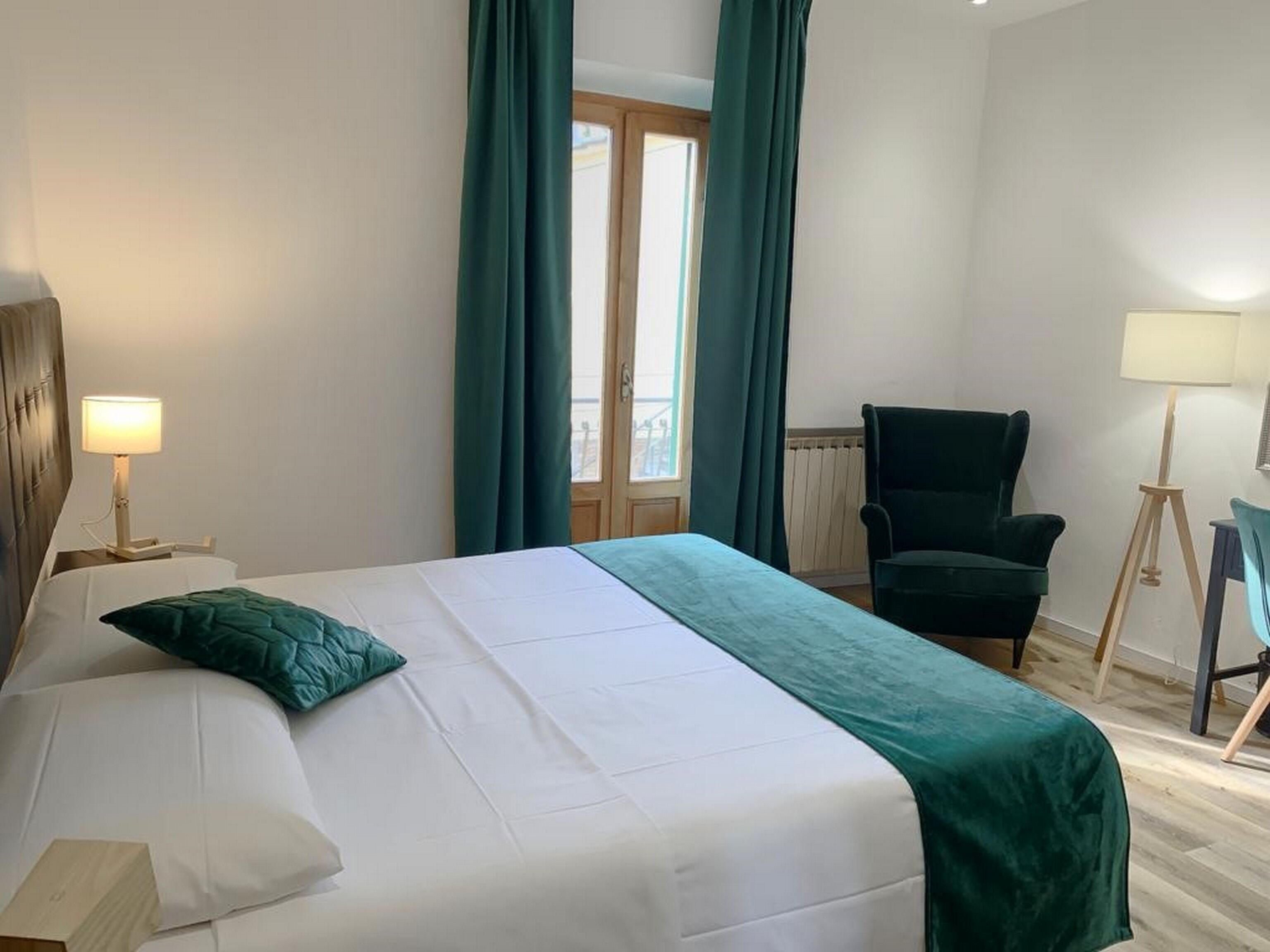 Ein Hotelzimmer mit Bett, Stuhl, Lampe und einem fenster mit Vorhängen.