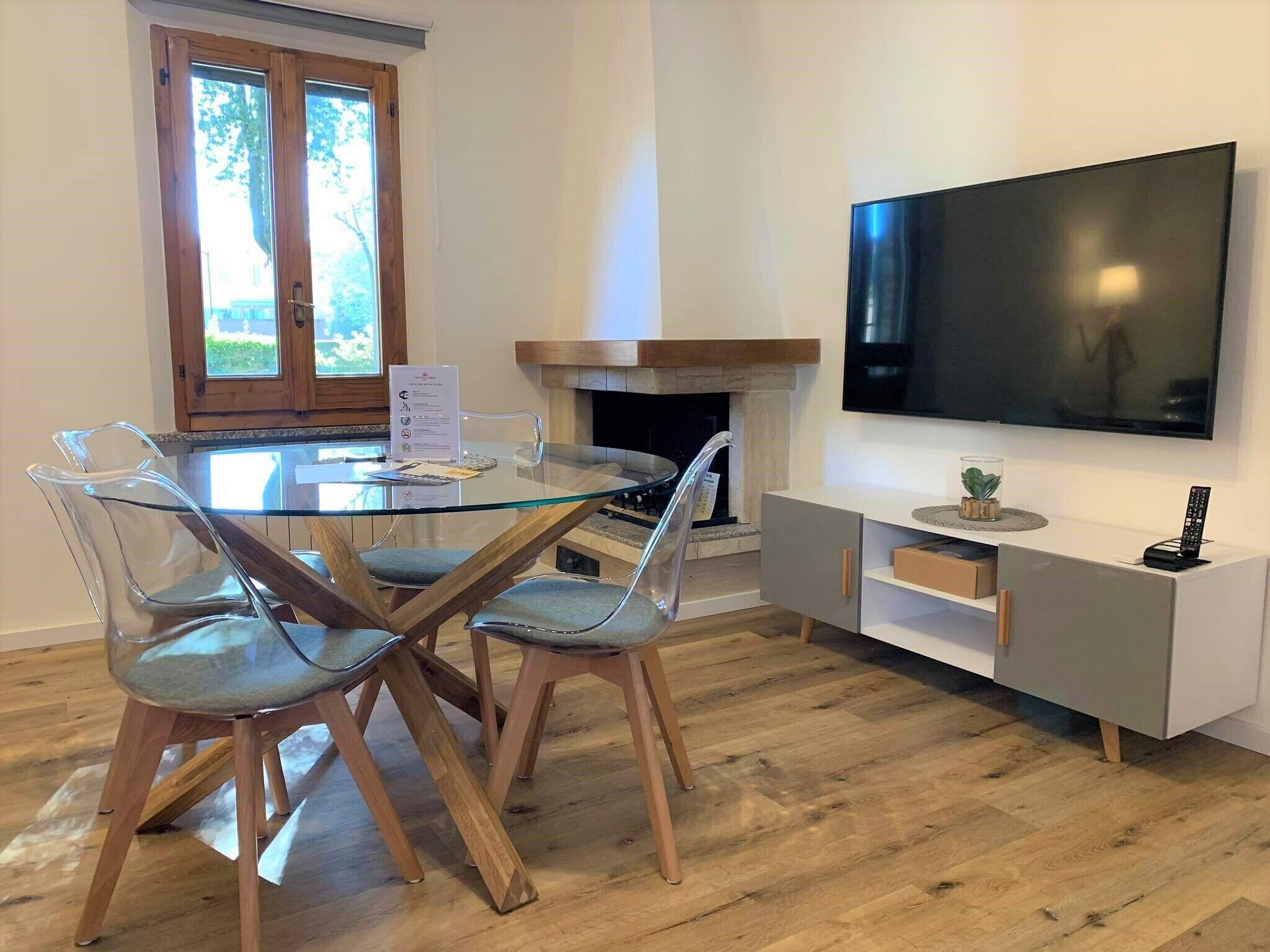 Un'area pranzo moderna con tavolo e sedie in vetro, un camino e una TV a parete.