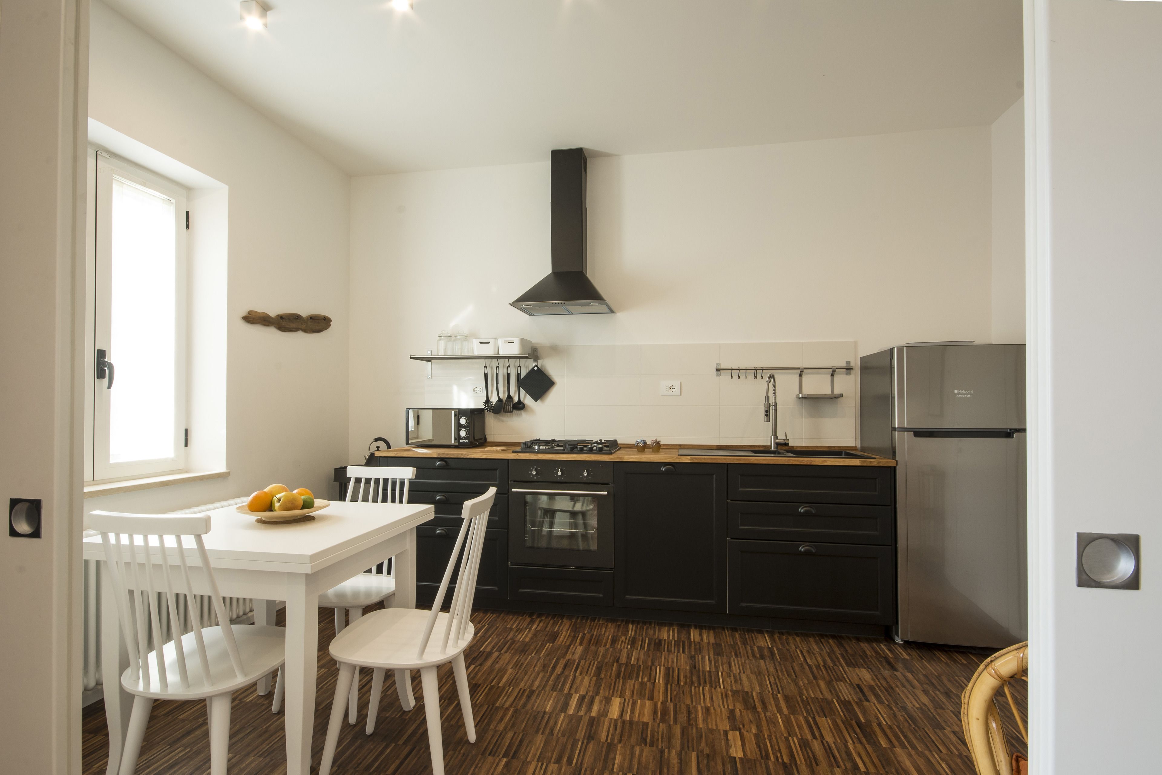 Une cuisine moderne avec des meubles blancs, une hotte noire et un réfrigérateur en acier inoxydable.