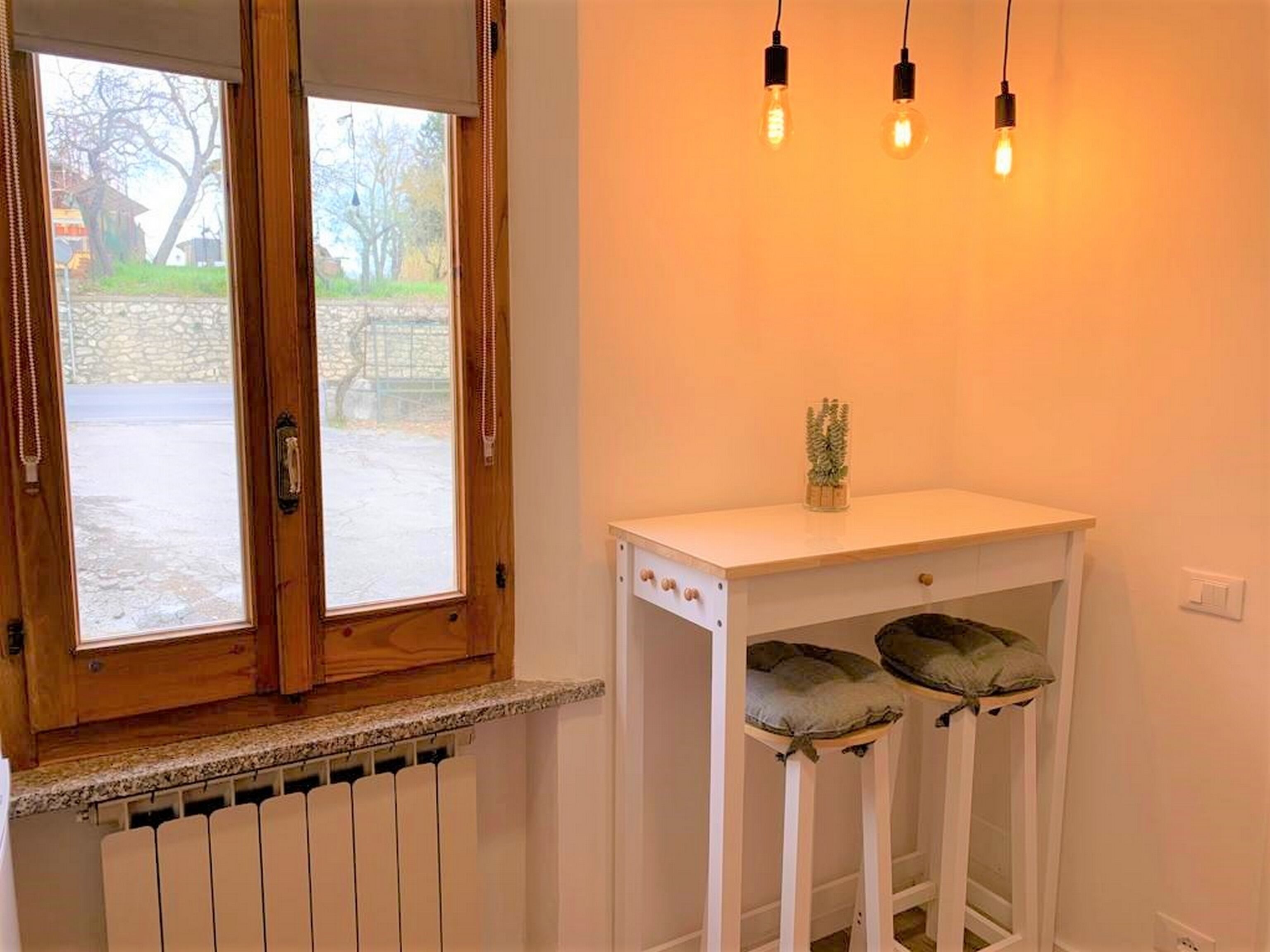 A room with a wooden-framed window, a white radiator, and a white console table with two cushioned stools.