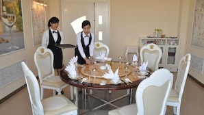 A dining area with a round table set for four, surrounded by white chairs. A server is attending to the table. - Phoenix Hotel (Hac Thanh)