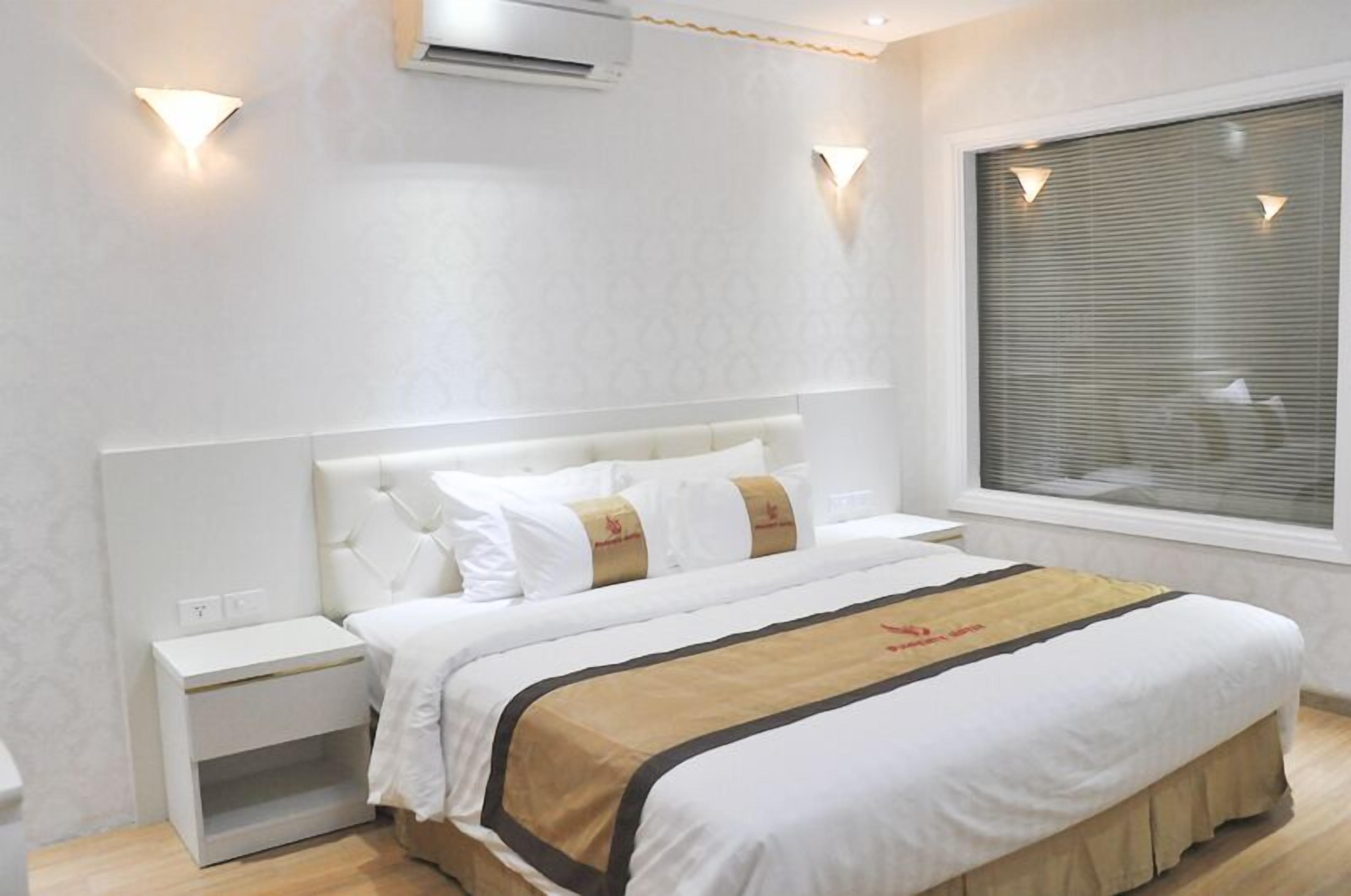 Moderni hotellihuone, jossa on suuri sänky, valkoiset seinät ja ikkuna, jossa on sälekaihtimet.