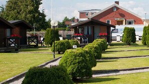 A row of wooden cabins with small front porches, each with a table and chairs. - Milano Garden - City Bungalow Hotell, i gränssnittet till Kullabygdens pärlor (Astorp)
