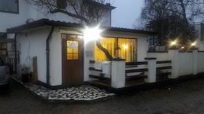 A small building with a wooden door and a window, a ramp leading to the entrance, and a tiled area in front. - Milano Garden - City Bungalow Hotell, i gränssnittet till Kullabygdens pärlor (Astorp)