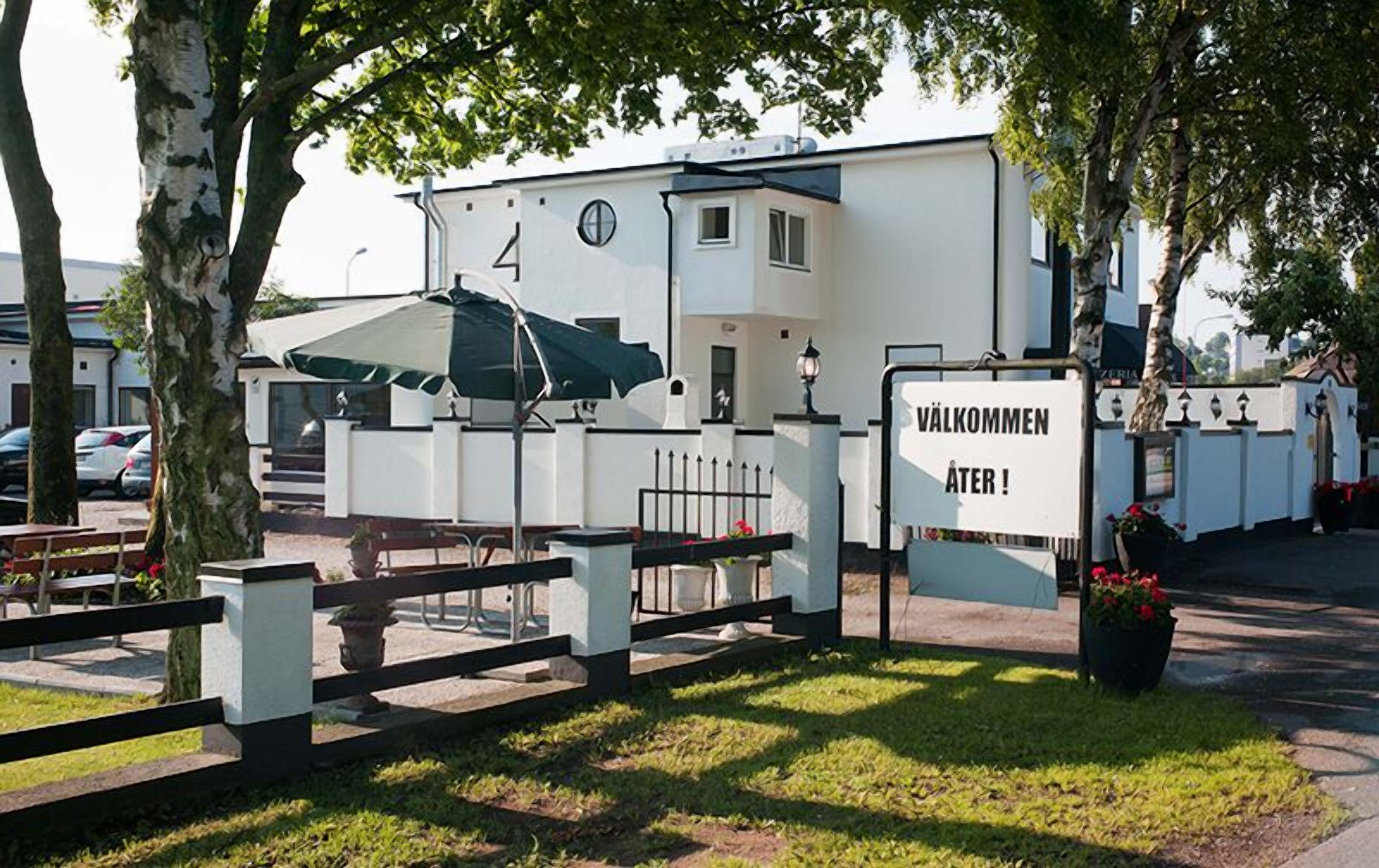 A building with a sign reading "VÄLKOMMEN ÅTER!" and a fenced area with outdoor seating.