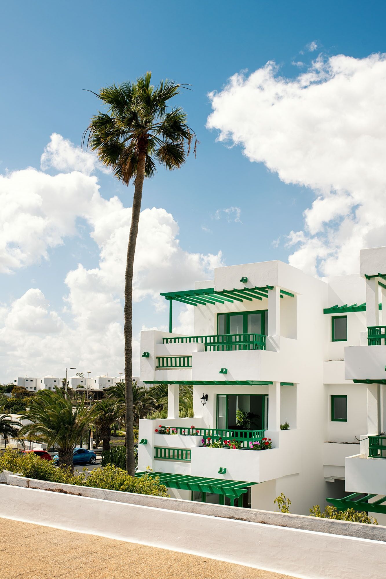 Un edificio moderno blanco con detalles en verde, con balcones y una palmera al fondo.