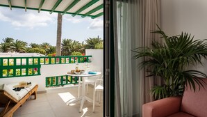 A balcony with a white table, chairs, and a small sofa. There is a large potted plant and a pink sofa inside the room. - Apartamentos Nazaret (Teguise)