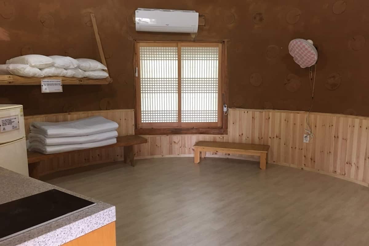 Een kamer met een houten vloer, een bankje, een raam met een rasterpatroon en een handdoekrek met opgevouwen handdoeken.