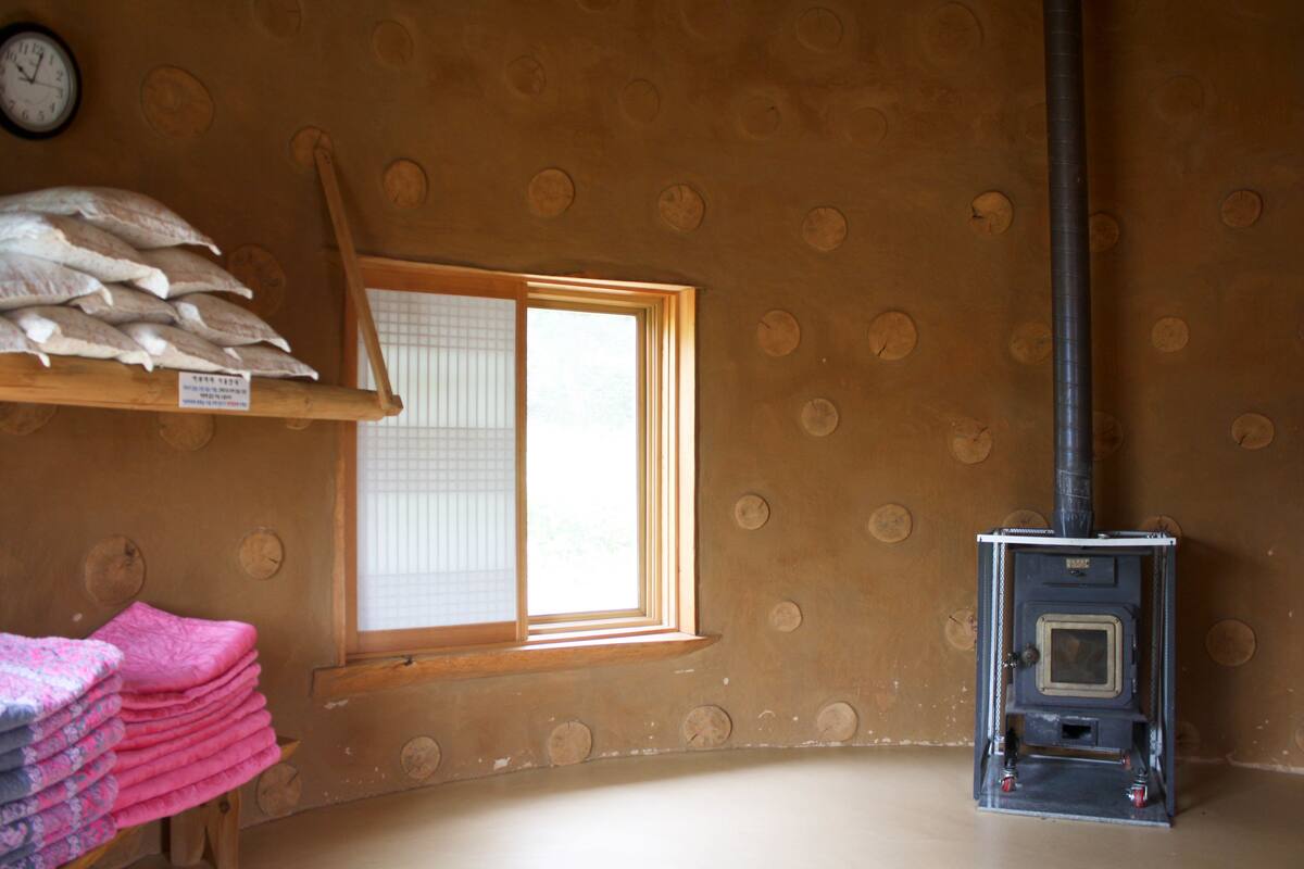 Een kamer met een raam, een wandklok, een plank met vissen, en een houtkachel.