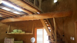 Un intérieur rustique en bois, agrémenté d’un ventilateur, d’étagères où sont pliées des couvertures et d’une fenêtre à carreaux.