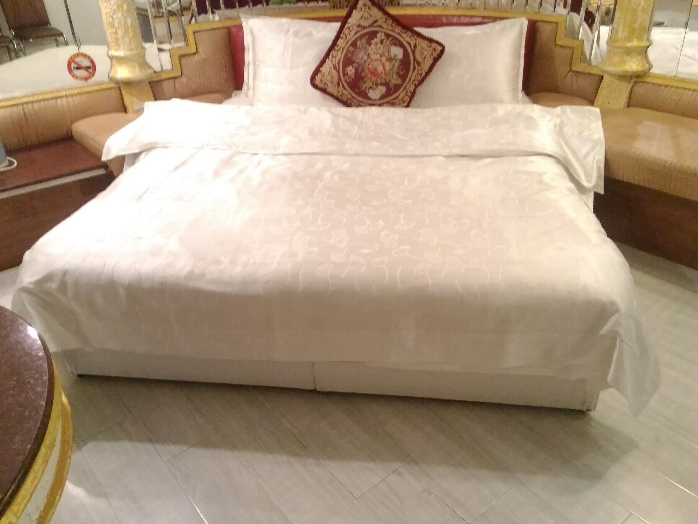 A large bed with a white bedspread and a decorative pillow, a beige sofa, and a marble floor.
